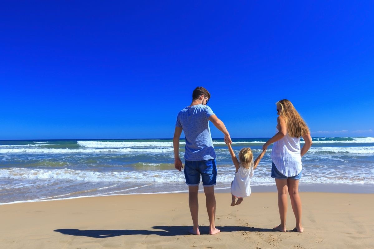 Happy father mother and little stand on the sea shore on a sunny day.COpy space, back view.